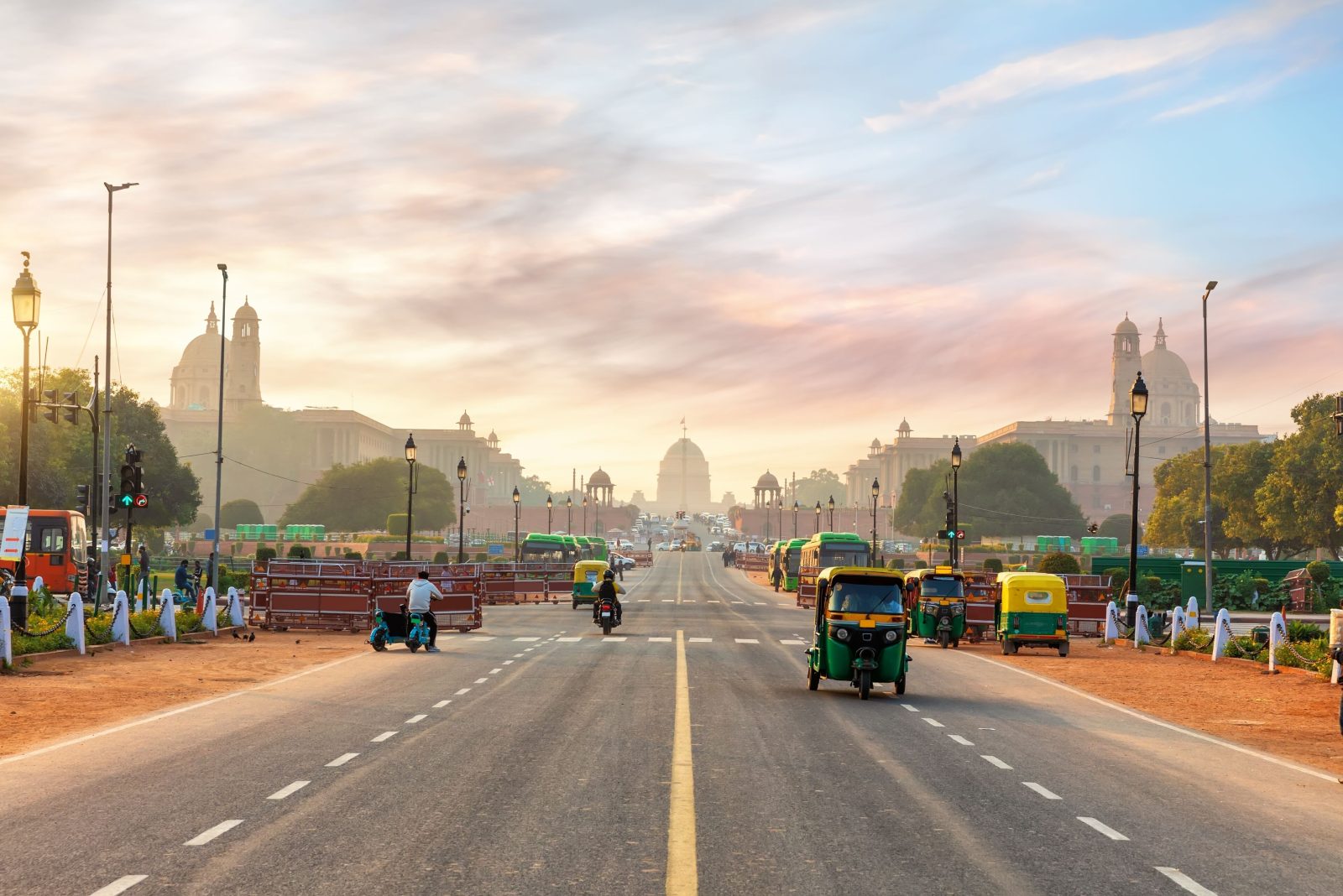 A avenida cerimonial de Nova Delhi ao amanhecer, com o palácio presidencial ao fundo e tuk-tuks em primeiro plano